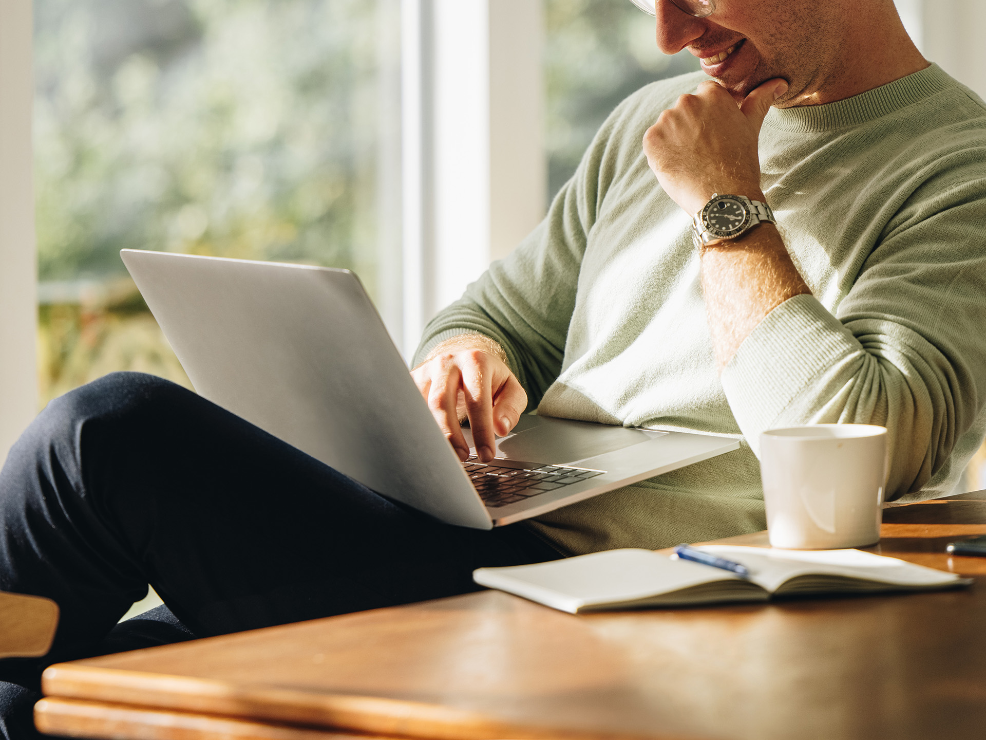 Man at home, using laptop, smiling.