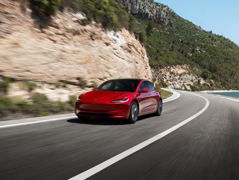 Red Tesla Model 3 driving by the coast