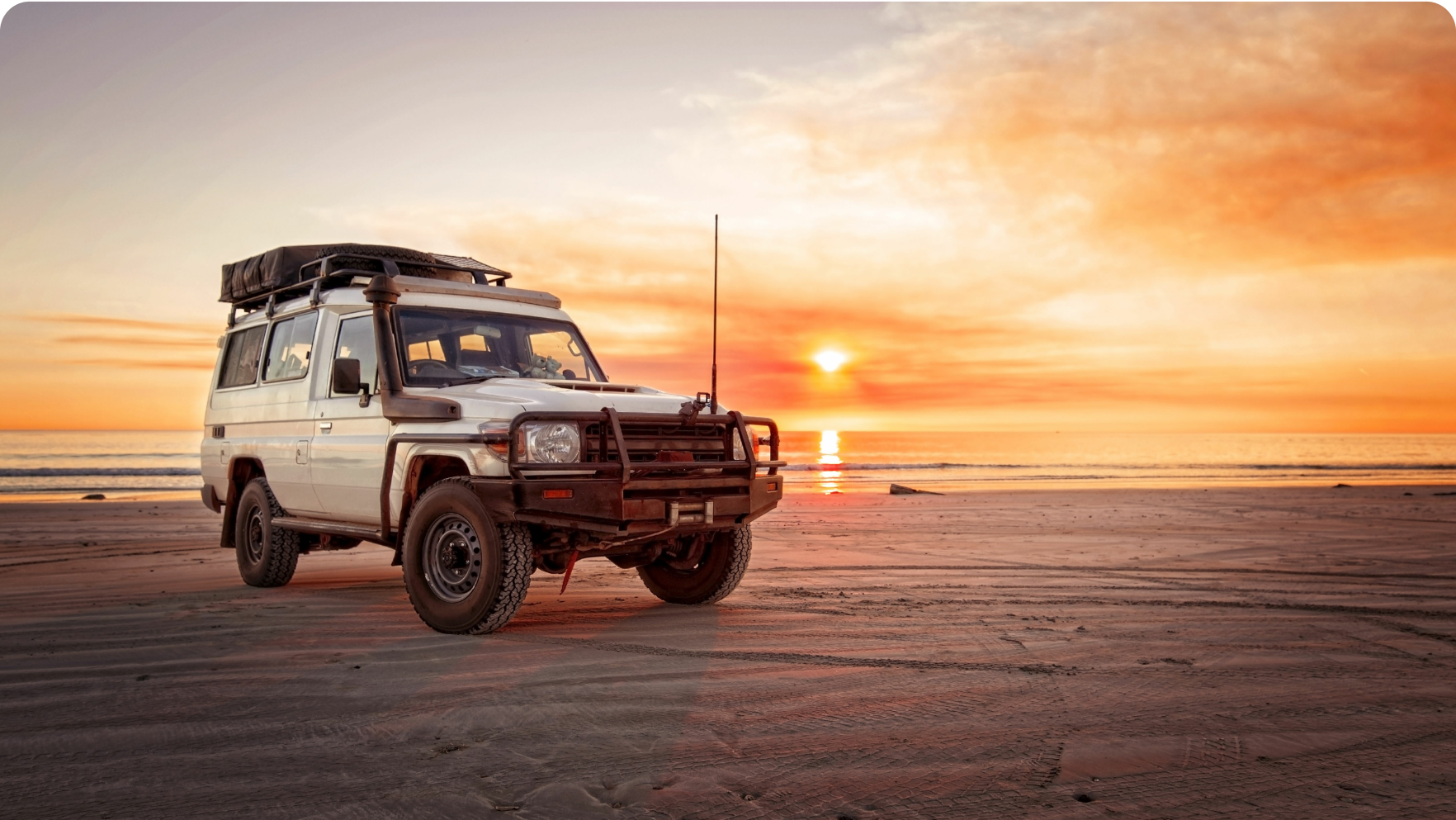 a 4 wheel drive on a beach with sunset in the background