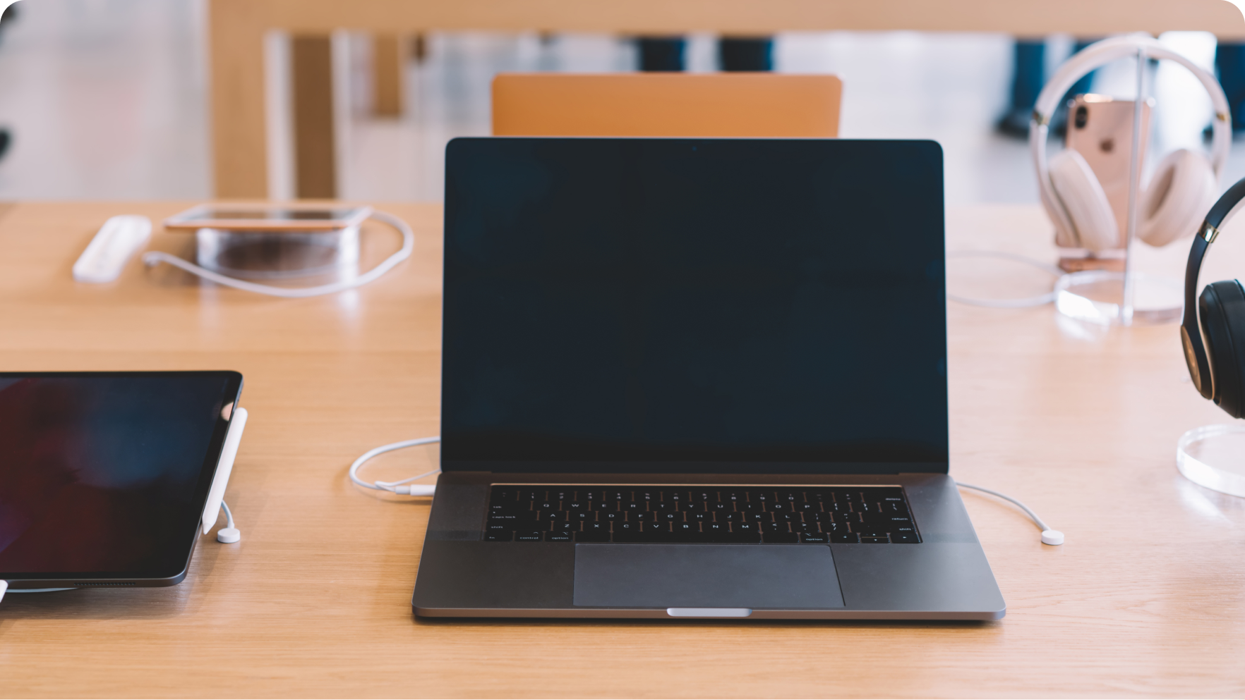 A laptop on a wooden table surrounded by other electronic devices