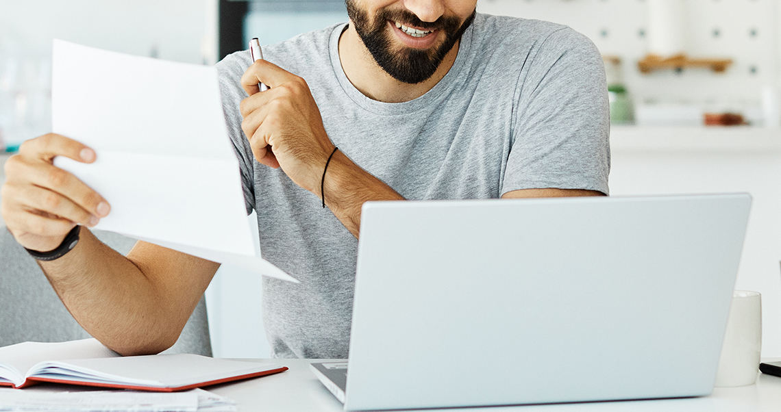Male looking at laptop paper in hand