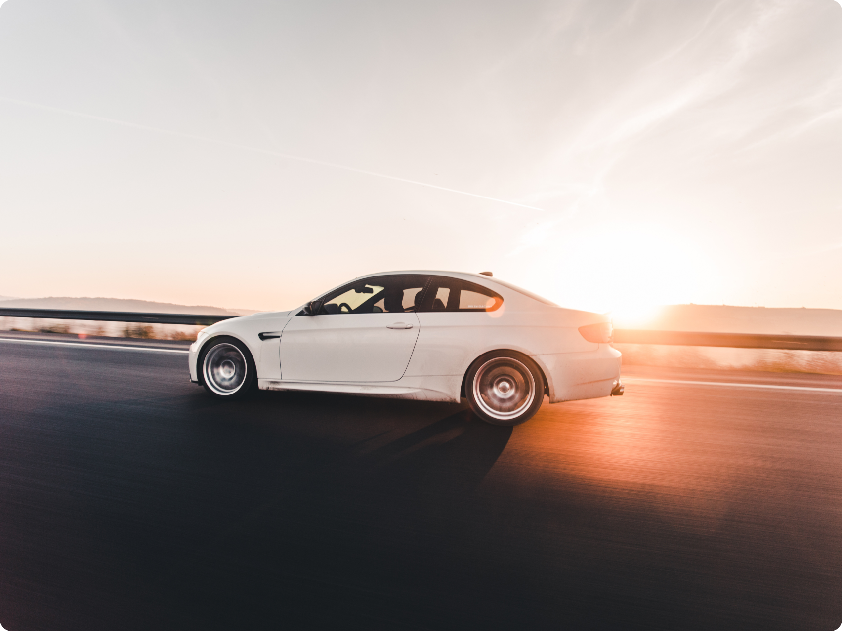 White car driving on a highway at sunset